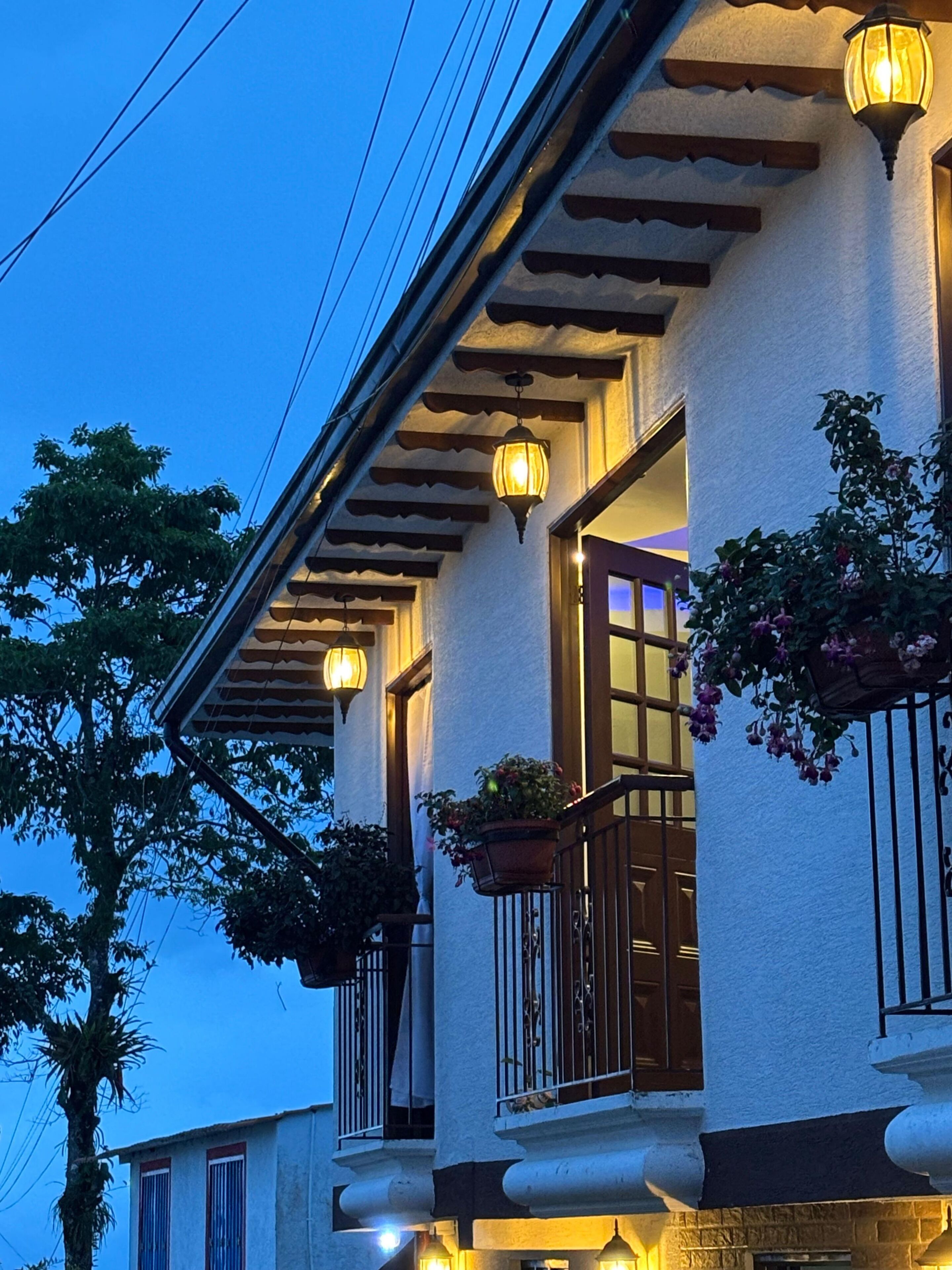 A building with a balcony, a window with a curtain, and a hanging flower pot.
