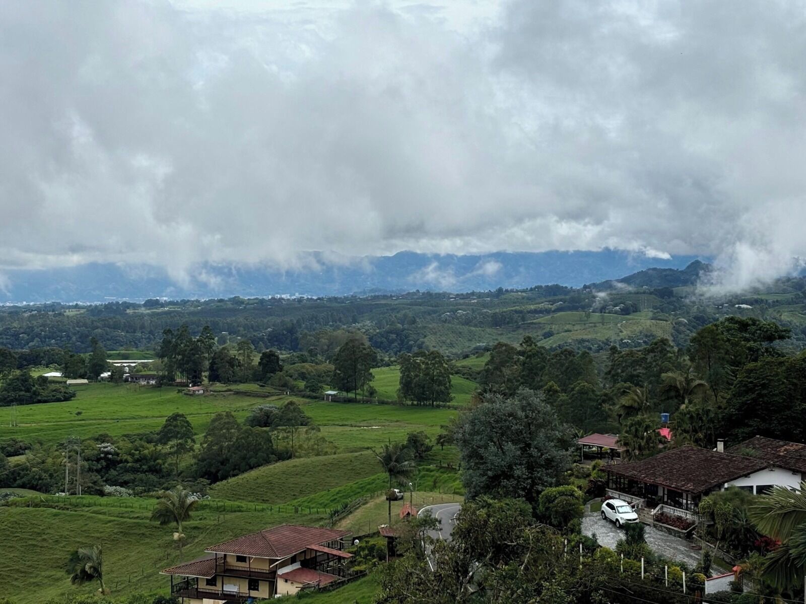 Un paisaje rural con colinas ondulantes, casas dispersas y un cielo nublado.