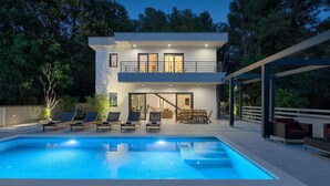 Une maison moderne à deux étages dotée d’une piscine, d’un espace salon extérieur et d’un patio couvert.