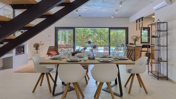 Un coin repas avec une table dressée pour quatre personnes, un escalier et une vue sur une piscine.