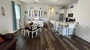Una cocina moderna con armarios blancos, una isla central y una zona de comedor con sillas blancas.