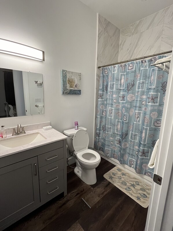 A bathroom with a white sink, a toilet, a mirror, and a shower curtain with a sea shell pattern. - New waterfront home, your peaceful getaway in Key Colony Beach, Marathon, FL (Key Colony Beach)