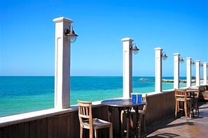 A seaside terrace with wooden chairs and tables, white pillars with lamps, and a view of the ocean. - New waterfront home, your peaceful getaway in Key Colony Beach, Marathon, FL (Key Colony Beach)
