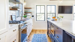 A modern kitchen with white cabinets, a stainless steel stove, and a blue patterned rug. - Renovated kitchen less than 2 miles to beach, walk to restaurants & bike trail (Harwich)