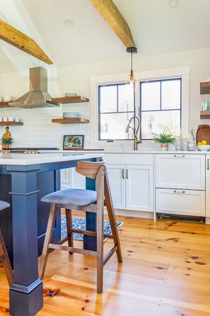 A modern kitchen with a large island, wooden bar stools, white cabinetry, and a large window providing natural light. - Renovated kitchen less than 2 miles to beach, walk to restaurants & bike trail (Harwich)
