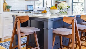 A modern kitchen with wooden beams, a large island with bar stools, and a view of the outdoors through large windows. - Renovated kitchen less than 2 miles to beach, walk to restaurants & bike trail (Harwich)