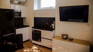 A compact kitchen with a built-in oven, microwave, and a large flat-screen TV mounted on the wall.