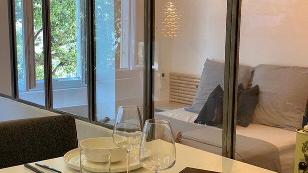 A dining area with a table set for four, a sofa with cushions, and a view of a balcony with trees.