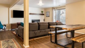 A modern living room with a sofa, a wooden coffee table, and a TV mounted on the wall. - Spacious 3BR Basement Apt | Airport, Work, Ski (North Salt Lake)