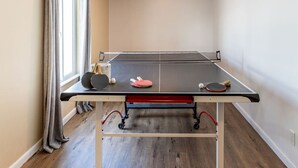 A ping pong table in a room with a window, curtains, and a ceiling light. - Spacious 3BR Basement Apt | Airport, Work, Ski (North Salt Lake)