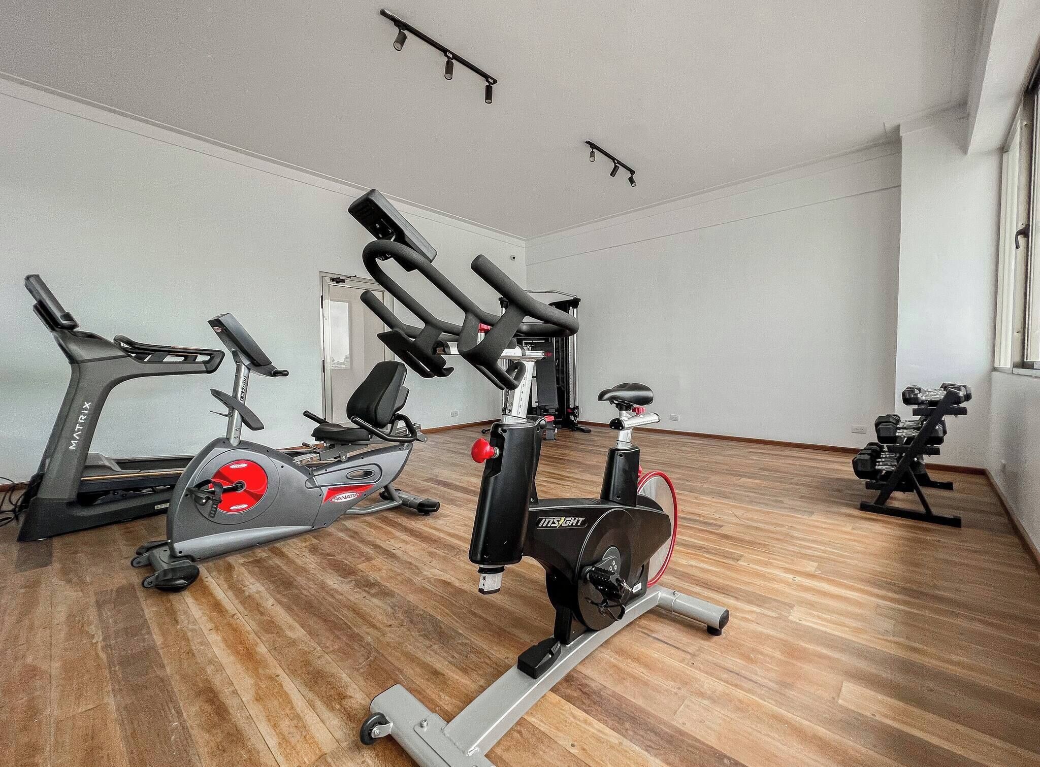 A gym with stationary bikes, a treadmill, and dumbbells.