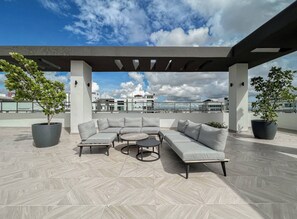 A rooftop patio with a sectional sofa, round table, and potted plants. - Goistay Elegant Refugio Caribeño 1br Gym Pool Naco APT 9F (Santo Domingo)