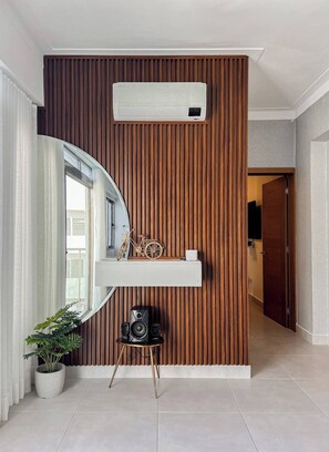 A modern interior with a wooden panel wall, a mounted air conditioner, a white console table with decorative items, a large mirror, and a potted plant. - Goistay Elegant Refugio Caribeño 1br Gym Pool Naco APT 9F (Santo Domingo)