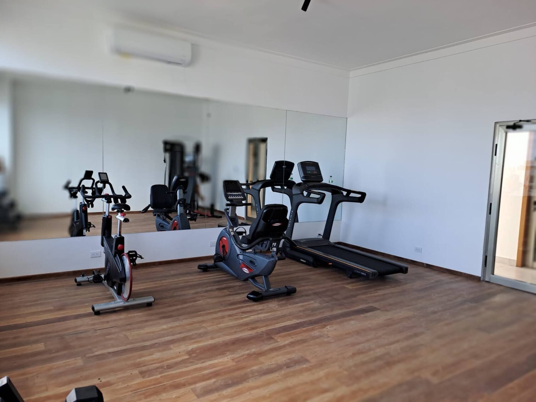 A gym with exercise equipment, a large mirror, and wooden flooring.