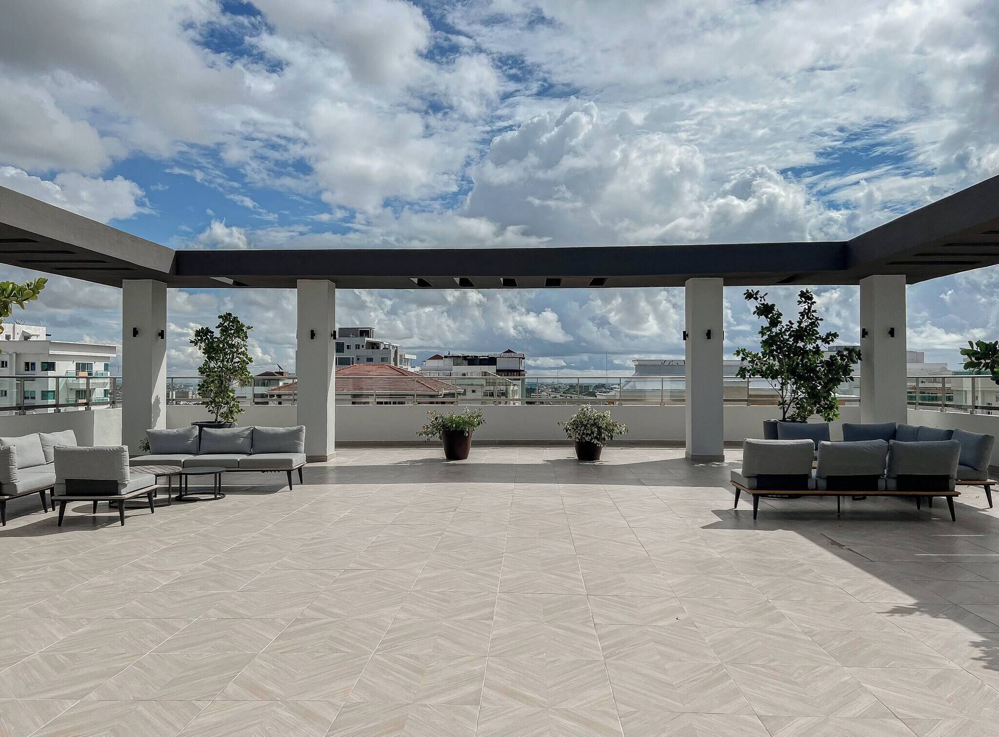 A rooftop terrace with a covered seating area, potted plants, and a view of the cityscape.