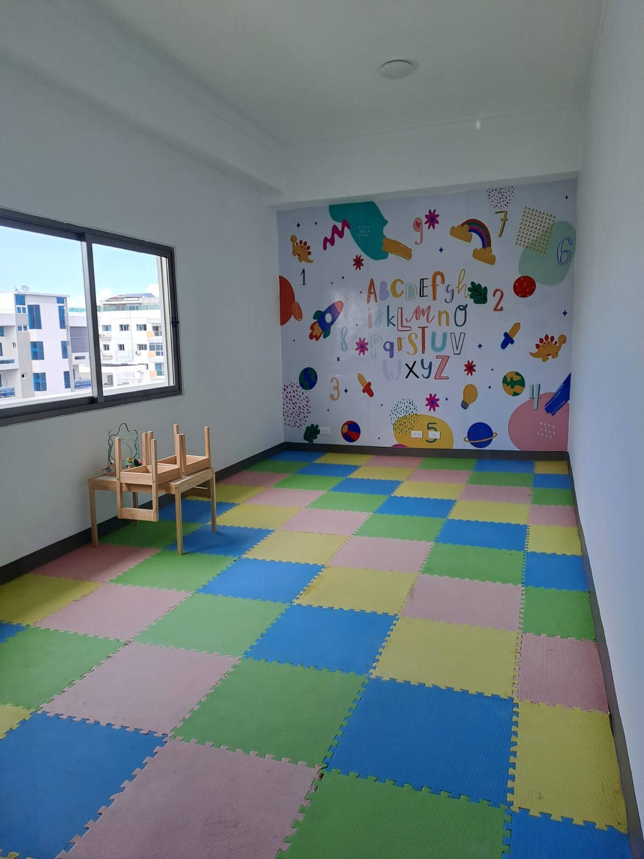 A room with a colorful floor, a window, and a wall with alphabet and number decorations.