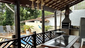 An outdoor patio with a wooden deck, a pool, and a barbecue grill. - Sobrado a 700 Metros Praia do Veloso (São Pedro Ilhabela)
