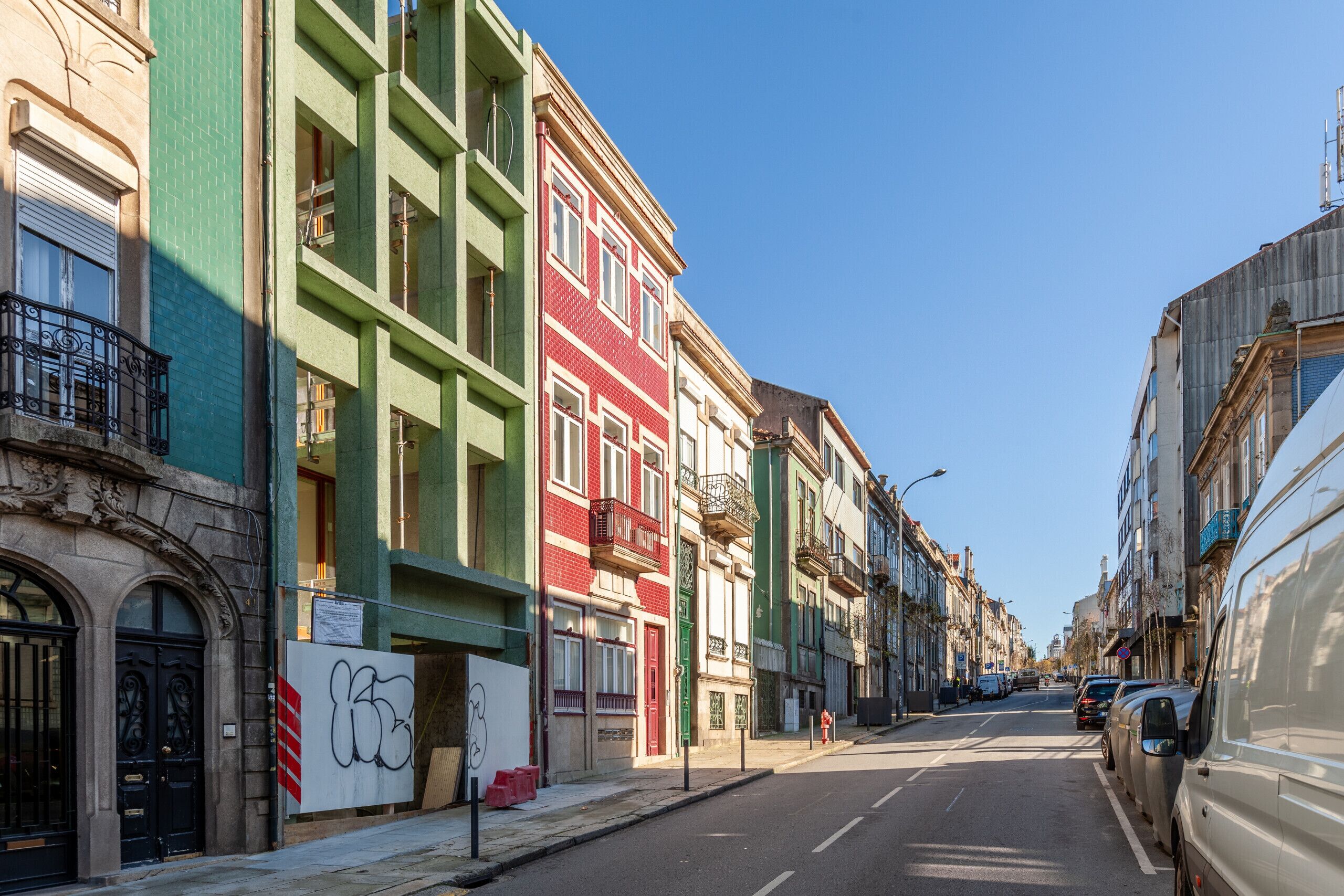 Una calle con edificios coloridos, cielo despejado y coches estacionados.