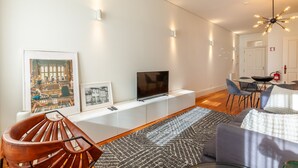 Un salon moderne avec un téléviseur à écran plat posé sur une console blanche, un tapis à motifs et un fauteuil marron.
