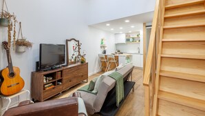 A modern living room with a television, wooden furniture, a guitar, and a kitchen in the background. - Foz Outeiro House 12 (Oporto)