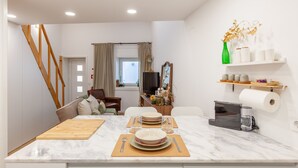 A modern kitchen with a marble countertop, wooden cutting board, and a dining area with a table set for four. - Foz Outeiro House 12 (Oporto)
