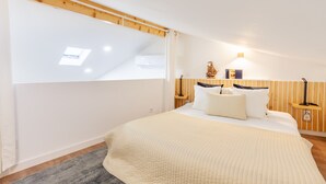 A bedroom with a sloped ceiling, a skylight, a bed with a quilted bedspread, two bedside tables with lamps, and a wooden headboard. - Foz Outeiro House 12 (Oporto)