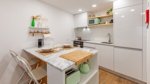 A modern kitchen with white cabinets, a marble countertop, a green kettle, and a microwave on a shelf. - Foz Outeiro House 12 (Oporto)