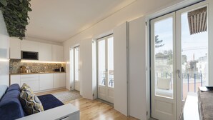 A modern kitchen with white cabinets, a microwave, and a patterned backsplash. There is a sliding glass door leading to a balcony with a view of the outside. - S. Bento Downtown Apt (Oporto)