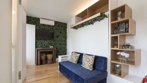 A modern living room with a blue sofa, wooden shelves, and a green wall. - S. Bento Downtown Apt (Oporto)