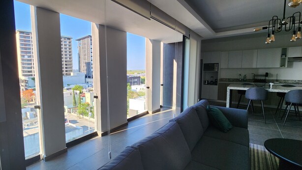 A modern living room with a large window, a sofa, and a dining area with chairs. - Depa Asoluta, Cerquita de TODO en el Norte de Mérida. CoWorking (Mérida)