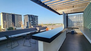 A rooftop terrace with a long counter, two black metal chairs, and a view of surrounding buildings. - Depa Asoluta, Cerquita de TODO en el Norte de Mérida. CoWorking (Mérida)