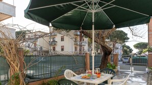 An outdoor patio with a table and chairs under a green umbrella, surrounded by a low stone wall and greenery. - Apartment Angela by Interhome (Follonica)