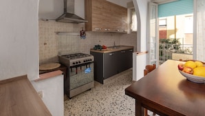 A modern kitchen with a gas stove, oven, and wooden cabinets. There is a window with a view of a balcony and a bowl of fruit on the table. - Apartment Angela by Interhome (Follonica)