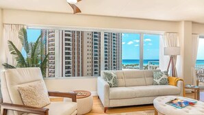 Sala de estar com sofá, poltrona, mesa de centro e vista para um arranha-céu e oceano.