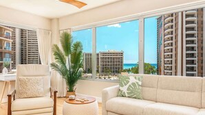 Uma sala de estar moderna com sofá, poltrona e mesa de centro, janelas amplas com vista para a cidade e um ventilador de teto.