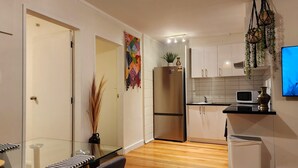 A modern kitchen with white cabinets, a stainless steel refrigerator, a microwave, and a small trash bin. - CQN's (Wellington)