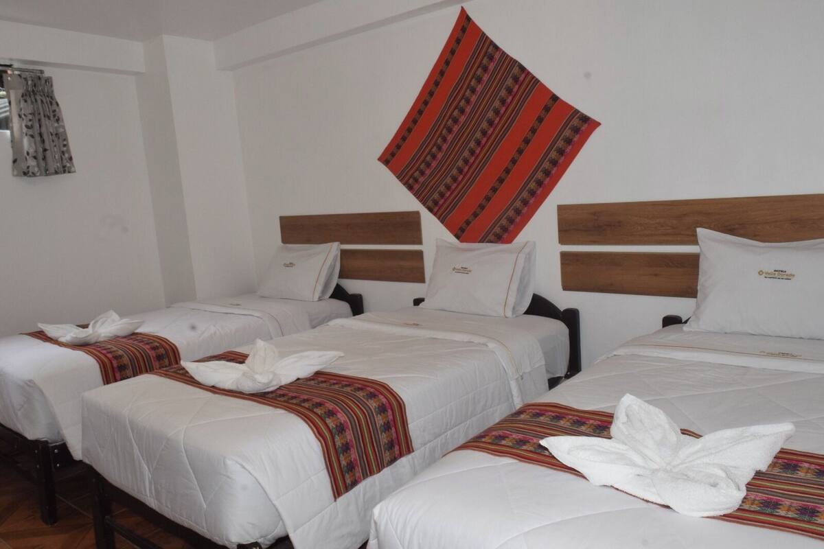 A hotel room with three single beds, each with a white duvet and a colorful blanket.
