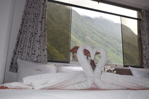 A hotel room with a bed, white towels, and a mountain view through large windows. - HOTEL VALLE DORADO MACHUPICCHU (Machu Picchu)