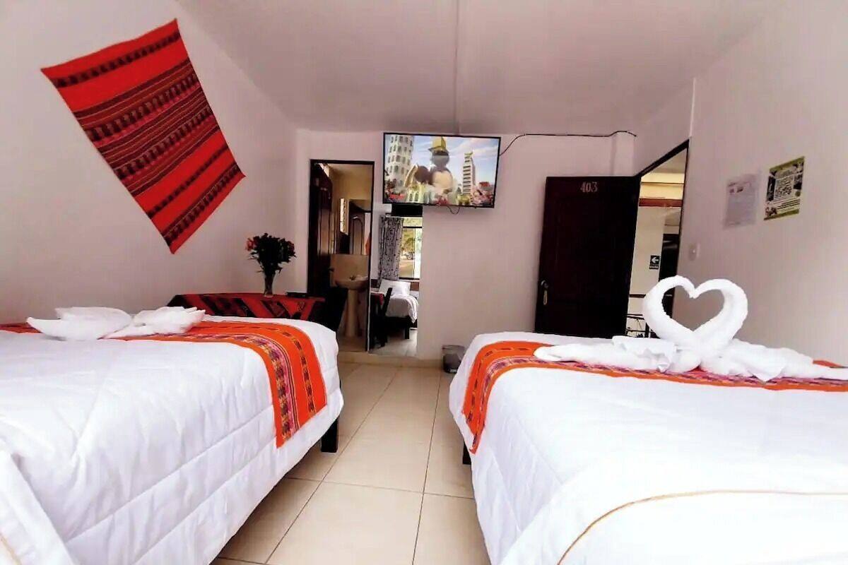 A hotel room with two beds, a TV mounted on the wall, and a red wall hanging.