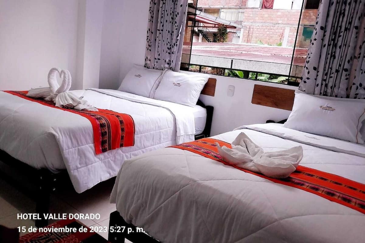 A hotel room with two beds, white bedding, and red decorative pillows.