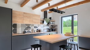 A modern kitchen with wooden beams, a large island with stools, and a view of the outdoors. - Awesome home in Vizinada (Vizinada)