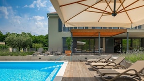 A poolside area with lounge chairs, a covered seating area, and a view of a modern building. - Awesome home in Vizinada (Vizinada)