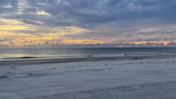 En strand med en bred sandstrand och ett lugnt hav under en molnig himmel.