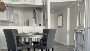 Ett modernt kök med vita skåp, ett matbord med stolar, en takfläkt och en skylt med texten ”Välkommen till vårt hus vid stranden”.
