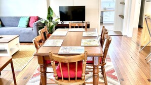 Un comedor con una mesa de madera, sillas y un televisor al fondo.