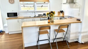 Una cocina moderna con encimera de madera, dos taburetes de bar, un microondas, un lavaplatos y una ventana con persianas.
