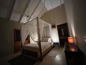 A bedroom with a four-poster bed, a ceiling fan, a bedside table with a lamp, and a window with blinds. - Las Terrenas - Caribbean Villa for 6 People - Exceptional Location (Las Terrenas)