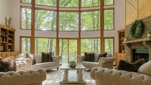 A spacious living room with a high ceiling, large windows, and a fireplace. - Cabin by the Bluff (Altamont)