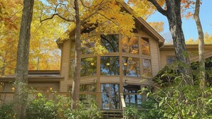 A multi-story house with large windows and a wooden exterior, surrounded by trees with autumn foliage. - Cabin by the Bluff (Altamont)