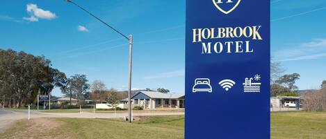 A sign for Holbrook Motel with a logo, name, and icons indicating amenities like a bed, Wi-Fi, and a pool.